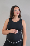 A pregnant woman wearing a black maternity tank top and matching black leggings with the brand name 'BIA+HERA' printed in white on the waistband, standing against a neutral gray background.
